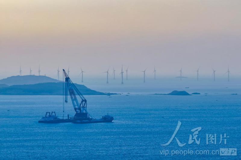 平潭综合实验区北岚岭附近海域，正在生产作业的风电安装船，与大海、晚霞、风车、渔船构成了一幅美丽画卷。