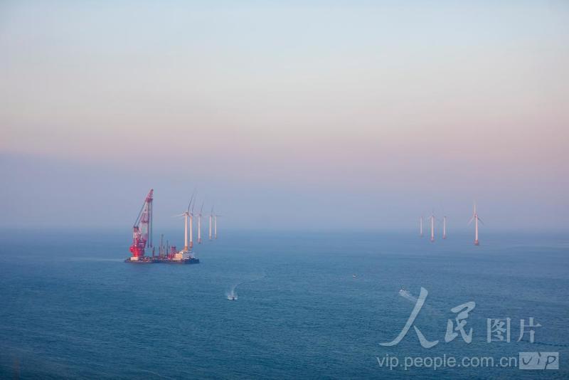 平潭综合实验区北岚岭附近海域，正在生产作业的风电安装船，与大海、晚霞、风车、渔船构成了一幅美丽画卷。