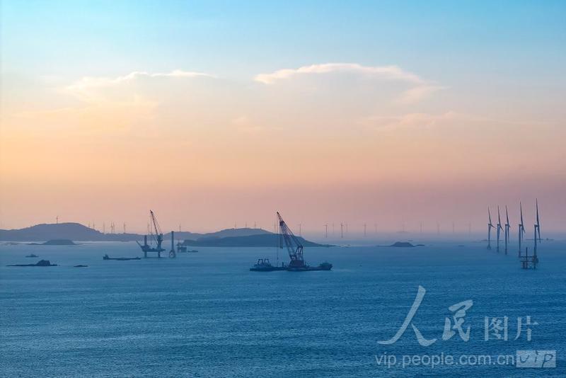 平潭综合实验区北岚岭附近海域，正在生产作业的风电安装船，与大海、晚霞、风车、渔船构成了一幅美丽画卷。