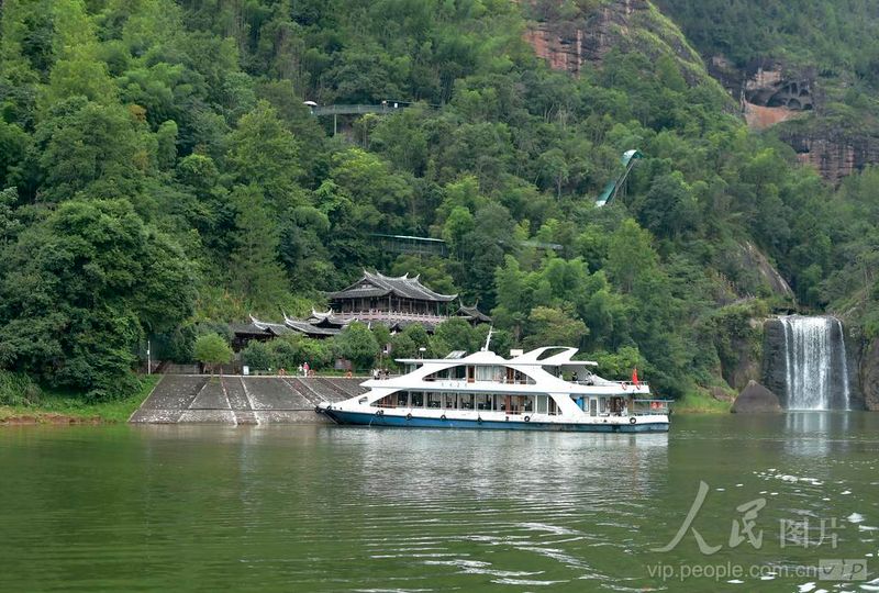 福建泰宁大金湖白水漈瀑布景点，游船航行湖面，古建飞瀑相映，尽显水上丹霞风光。
