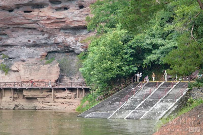 泰宁大金湖景区，层状丹霞巨石临水而立，游人沿着步道游览独特的丹霞地貌景观。