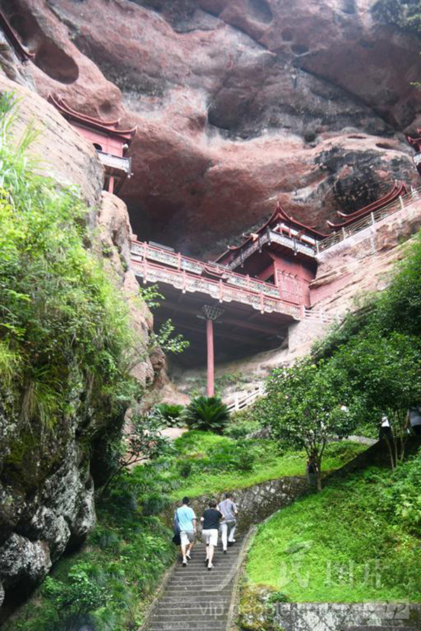 泰宁大金湖甘露寺古刹，依丹霞岩壁而建，一根木柱支撑楼阁，游人沿着石阶前往参观。
