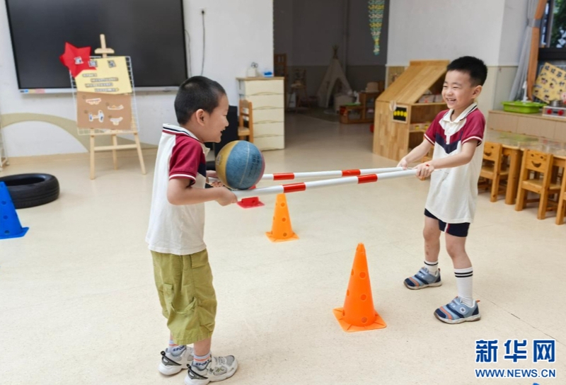 9月1日，福州延安中学集团延安幼儿园开展红色集星闯关活动，开启充满仪式感的新学期。图为两名小朋友齐心协力用横杆运球绕过障碍。新华网发（福州延安中学集团延安幼儿园供图）